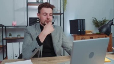 Businessman working on laptop computer wearing headset, freelance worker call center or support service operator helpline, having pleasant talk with client or colleague communication support at office