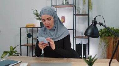 Başörtüsü takmış genç Müslüman iş kadını cep telefonuyla yazı yazarak 