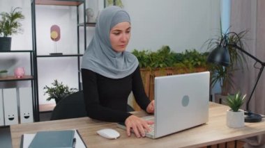 Türban takan genç Müslüman kadın başörtüsü açılır dizüstü bilgisayar çalışmaya başlar mesajlar gönderir, internetten alışveriş yapar, film izler. Arap kız modern ofis çalışma alanında dizüstü bilgisayar kullanıyor