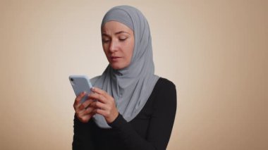 Mutlu, heyecanlı, tesettürlü, neşeli Müslüman kadın cep telefonu kullanıyor. 