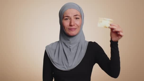 お金のキャッシュレスを転送するプラスチッククレジットカードの広告を示す幸せなイスラム教徒の女性は オンラインショッピング販売割引 インターネット注文配信購入を購入します 若いです女の子オンベージュ背景 — ストック動画