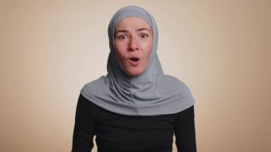 Aman Tanrım, vay canına. Heyecanlı Müslüman kadın şaşkınlıkla el kaldırıyor büyük gözlerle kameraya bakıyor, ani zaferden şok oluyor. Samimi genç kız bej renkli stüdyo arka planında tek başına.