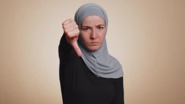 Hoşlanmamak. Üzüntülü, tesettürlü, tesettürlü, mutlu olmayan, hoşnutsuz, hoşnutsuz, hoşnutsuz, işaret işareti yapan mutsuz Müslüman kadın. Genç yetişkin bir kız. Bej arka planda kapalı stüdyo çekimleri