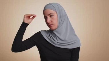 Müslüman milenyum kadını tesettür içinde elleri ve yuvarlanan gözleriyle saçma sapan jestler yapıyor, dedikodular, boş vaatler, vs. vs. Yalancılar! Genç Arap kız bej renkli stüdyo arka planında izole edilmiş.