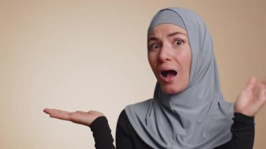 Müslüman milenyum kadınlarının tesettüre başparmak göstermesi ve boş yerleri göstermesi ticari metinler için reklam alanı, ürün tanıtımı için kopyalama alanı. Genç bir kız. Bej arka planda kapalı alan çekimleri