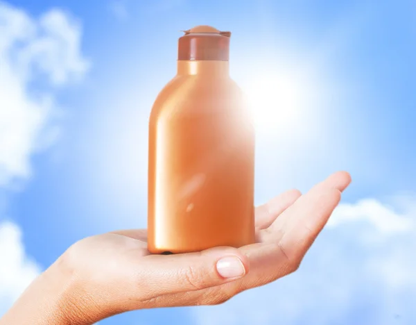Hand holding plastic bottle for sun lotion against blue sky.