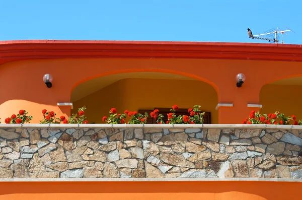 Kleurrijke typisch Sardijnse huis met de rode bloemen en blauwe hemelachtergrond, oranje huis fragment close-up in zonnige dag, kleurrijke Sardijnse huis, mooi gebouw in porto torres, Sardinië, Italië, — Stockfoto