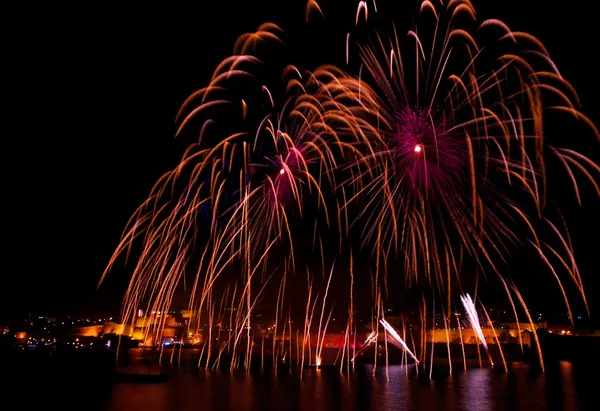 Fireworks, colorful different colors, amazing fireworks with city background in Valletta, Malta, dark sky background and house light in the far, Malta fireworks festival, 4 of July, Independence day — Stock Photo, Image