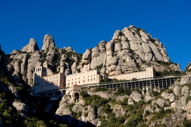 Montserrat Monastery is spectacularly Benedictine Abbey in the mountains near Barcelona, Catalonia,Spain.Montserrat.Panorama of the Monastery de Montserrat against background of mountains with shadows clipart