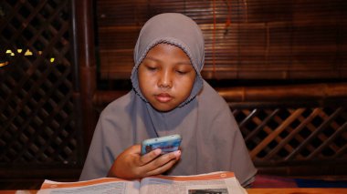 Kitap okurken tesettürlü bir kız ama cep telefonuna bakıyor, Batang, Endonezya, 9 Nisan 2022