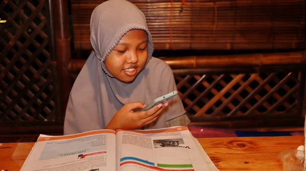 Dziewczyna Hidżabie Podczas Nauki Książki Ale Patrząc Telefon Komórkowy Batang — Zdjęcie stockowe