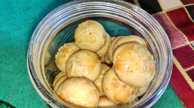 Nastar or indonesian pineapple tart cookies in glass jar on wooden tray with a cup of tea and a jar of nastar as background .very popular for serving to celebrate Eid/idul fitri.