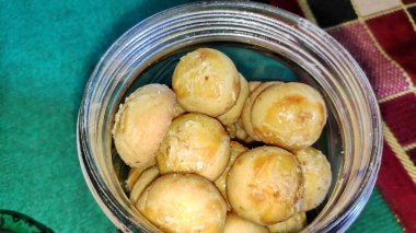 Nastar or indonesian pineapple tart cookies in glass jar on wooden tray with a cup of tea and a jar of nastar as background .very popular for serving to celebrate Eid/idul fitri.