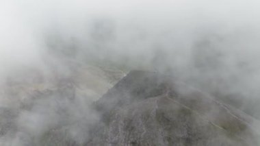 Carrauntoohil 'in havadan görünüşü, dağın tepesindeki insanlar, ışık bulutlu, haçın etrafında daireler çiziyor, 4k video.