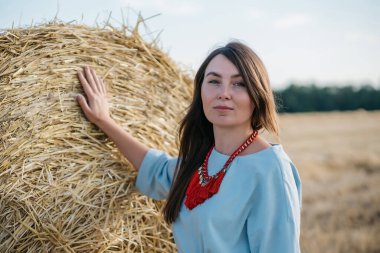 Gün batımında samanlığın yanındaki samanlığın yanında kırmızı kolyeli mavi elbiseli güzel bir esmer. Yüksek kalite fotoğraf