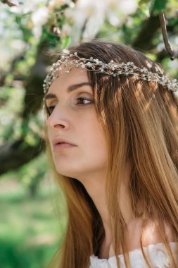 Güneşli bir bahar gününde, bir elma bahçesinde başında taç olan beyaz elbiseli güzel bir kızın portresi. Yüksek kalite fotoğraf