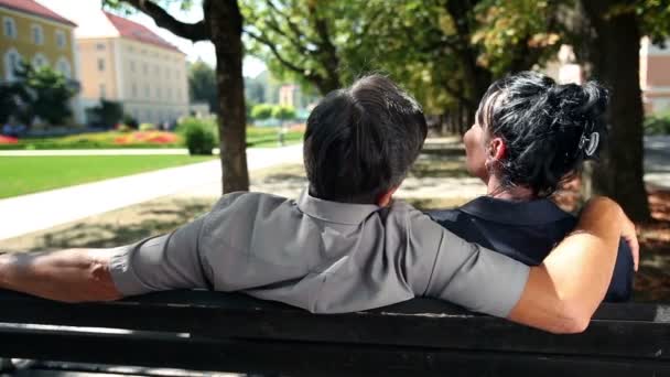 Фотография пары, сидящей на скамейке в парке в прекрасный летний день — стоковое видео