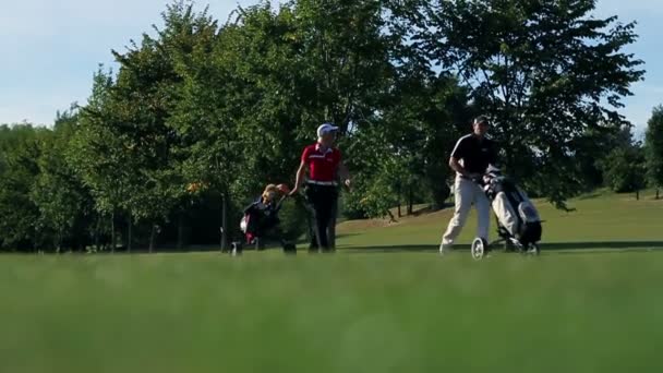 Tourné d'un coouple qui va sur l'autre terrain de golf prenant soin de tout l'équipement de golf — Video