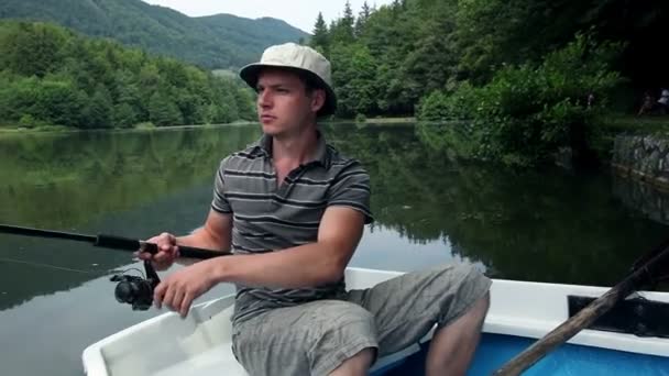 Un jeune homme pêche dans un bateau — Video