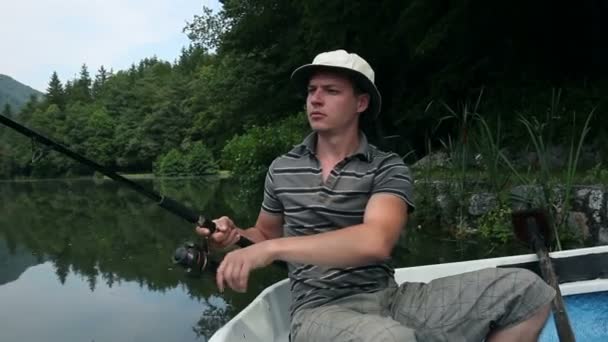 Joven pescando en un barco cerca del bosque — Vídeos de Stock