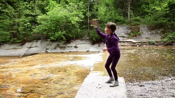 Tiro de niña lanzando piedras en el río — Vídeo de stock