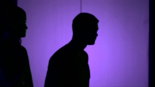 Άνδρες και γυναίκες που περπατούν μπροστά από το μοβ φως, έτσι ώστε να μπορούμε να δούμε τις σκιές τους — Αρχείο Βίντεο