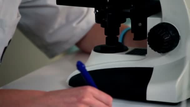 Woman looking through a microscope and examines — Stock Video