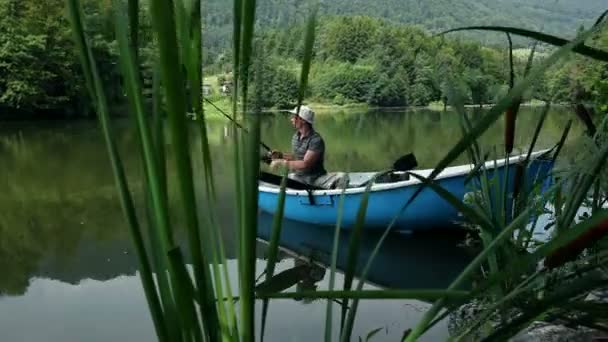 Młody człowiek, wędkowanie z łodzi w otoczeniu pięknej przyrody — Wideo stockowe