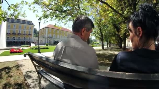 Skott av ett par sitter på en parkbänk på en beuatiful sommardag — Stockvideo