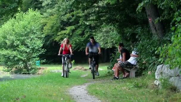 Jong koppel fietsen in de natuur en passerende familie die zit op de Bank — Stockvideo