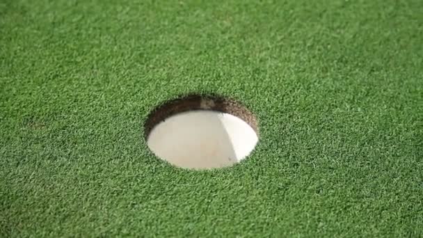 Primer plano de una sala y pelota de golf blanca que va directamente a la sala y una mano de golfistas que recoge una pelota de golf — Vídeos de Stock