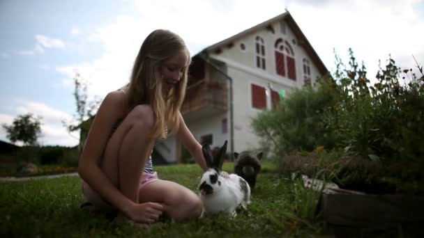 Tonårig flicka smekande kaniner framför huset — Stockvideo