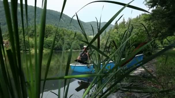 Young man fishing in the boat and a couple cycling near on pond — Stock Video