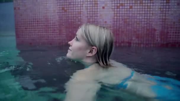 Красивая молодая женщина в открытом бассейне во время снега — стоковое видео