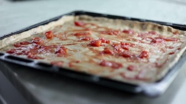 Close-up shot van een zwart blad met deeg en een persoon die op verschillende soorten ingrediënten voor pizza zet bakken — Stockvideo