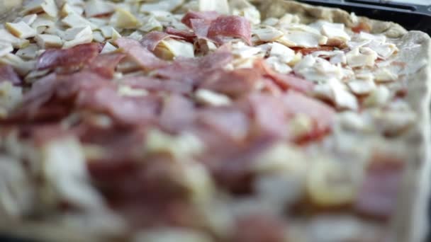 Nahaufnahme eines schwarzen Backblechs mit Teig und einer Person, die verschiedene Zutaten für Pizza anlegt — Stockvideo