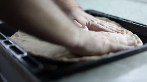 Gros plan d'une plaque à pâtisserie noire et l'homme met de la pâte et l'arrange autour de la pizza de la plaque à pâtisserie — Video