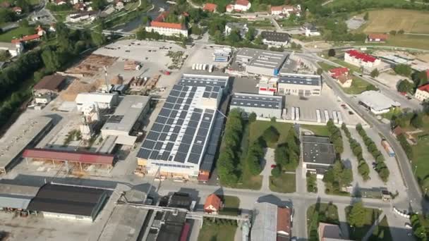 Helikopterista ammuttu panoraama, joka edustaa pienen kaupungin teollista osaa, jossa on aurinkovoimaloiden peittämiä kattoja — kuvapankkivideo