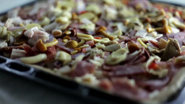 Close-up shot van een zwart blad met deeg en een persoon die op verschillende soorten ingrediënten voor pizza zet bakken — Stockvideo
