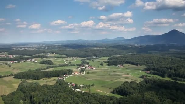 Vue panoramique depuis un hélicoptère représentant une vallée avec des champs, des prairies, une forêt et peu de maisons — Video