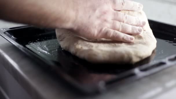 Gros plan d'une plaque à pâtisserie noire et l'homme met de la pâte et l'arrange autour de la pizza de la plaque à pâtisserie — Video