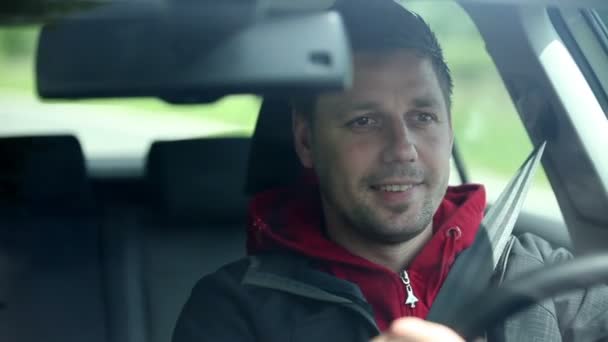 Hombre conduciendo coche y sonriendo a los transeúntes — Vídeo de stock