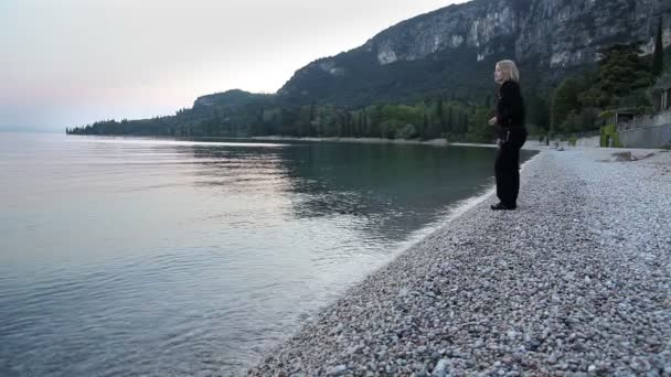 Mujer lanzando piedras al mar al amanecer — Vídeos de Stock