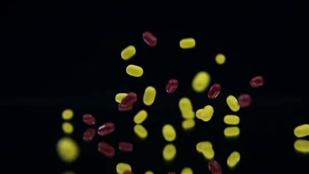 Red and yellow candies falling on mirror on black background in slow motion — Stock Video