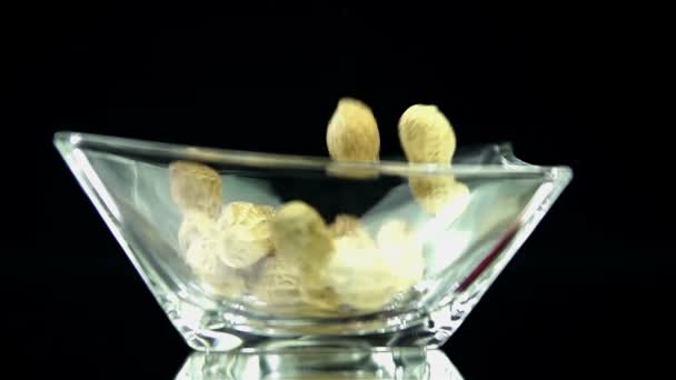 Los cacahuetes están cayendo en el vidrio en cámara lenta sobre fondo negro — Vídeos de Stock