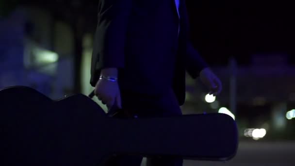 在漆黑的夜晚，在慢动作中携带一把吉他的男人 — 图库视频影像