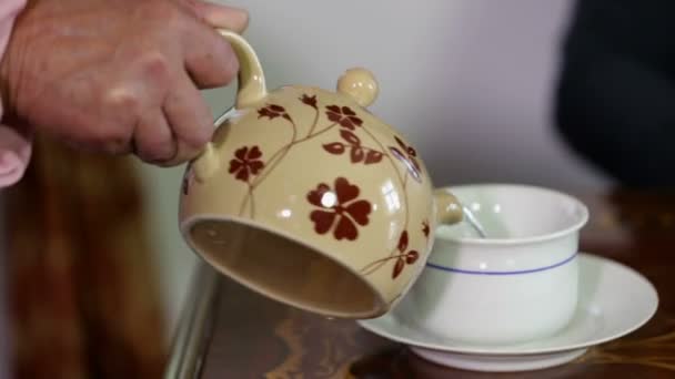 Velha senhora com mão tremendo derramando um chá em uma xícara — Vídeo de Stock