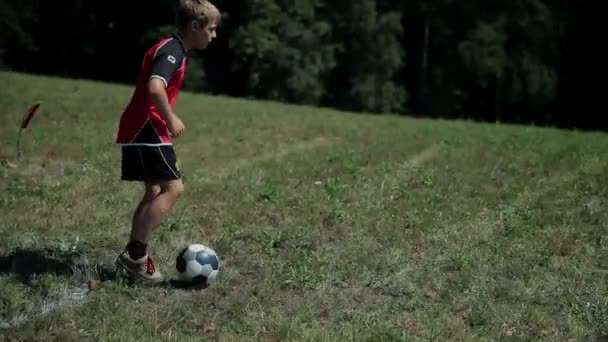 Criança liderando uma bola de futebol e caindo na grama — Vídeo de Stock