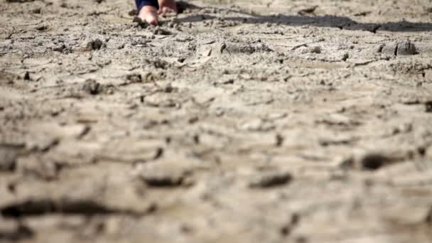 カメラに向かってひびの入った土の上を歩いて裸足の人 — ストック動画