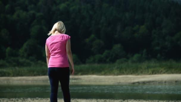 Jeune femme en robe rose et lunettes de soleil visitant une rivière — Video